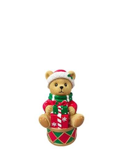 Cute Christmas teddy bear wearing a Santa hat and green scarf, sitting on a colorful drum while holding wrapped gift boxes.